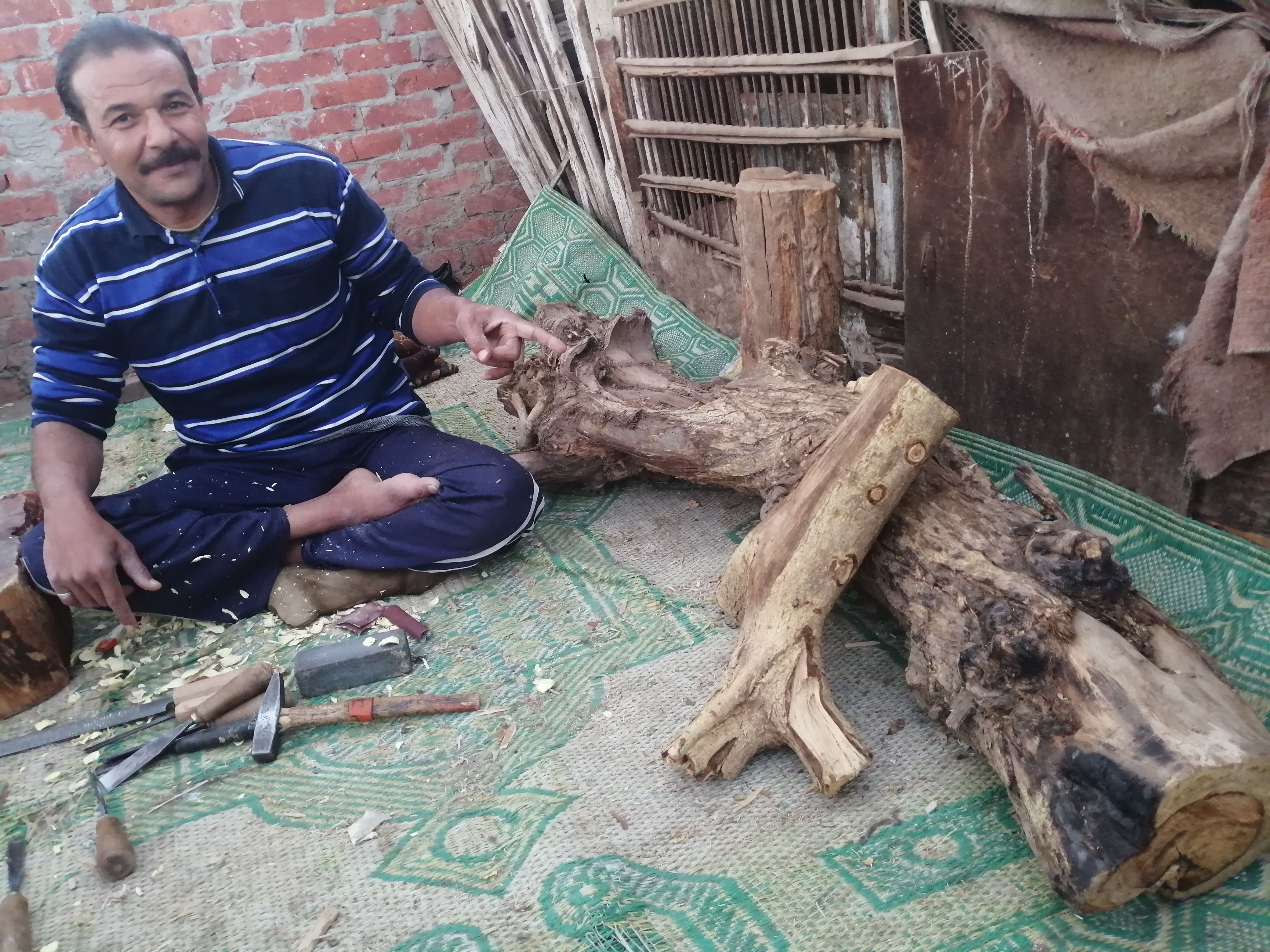 احمد وبجواره الاخشاب التى ينحت منها التماثيل